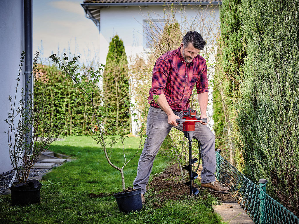 A man drills a hole in the garden soil with the Einhell cordless auger.